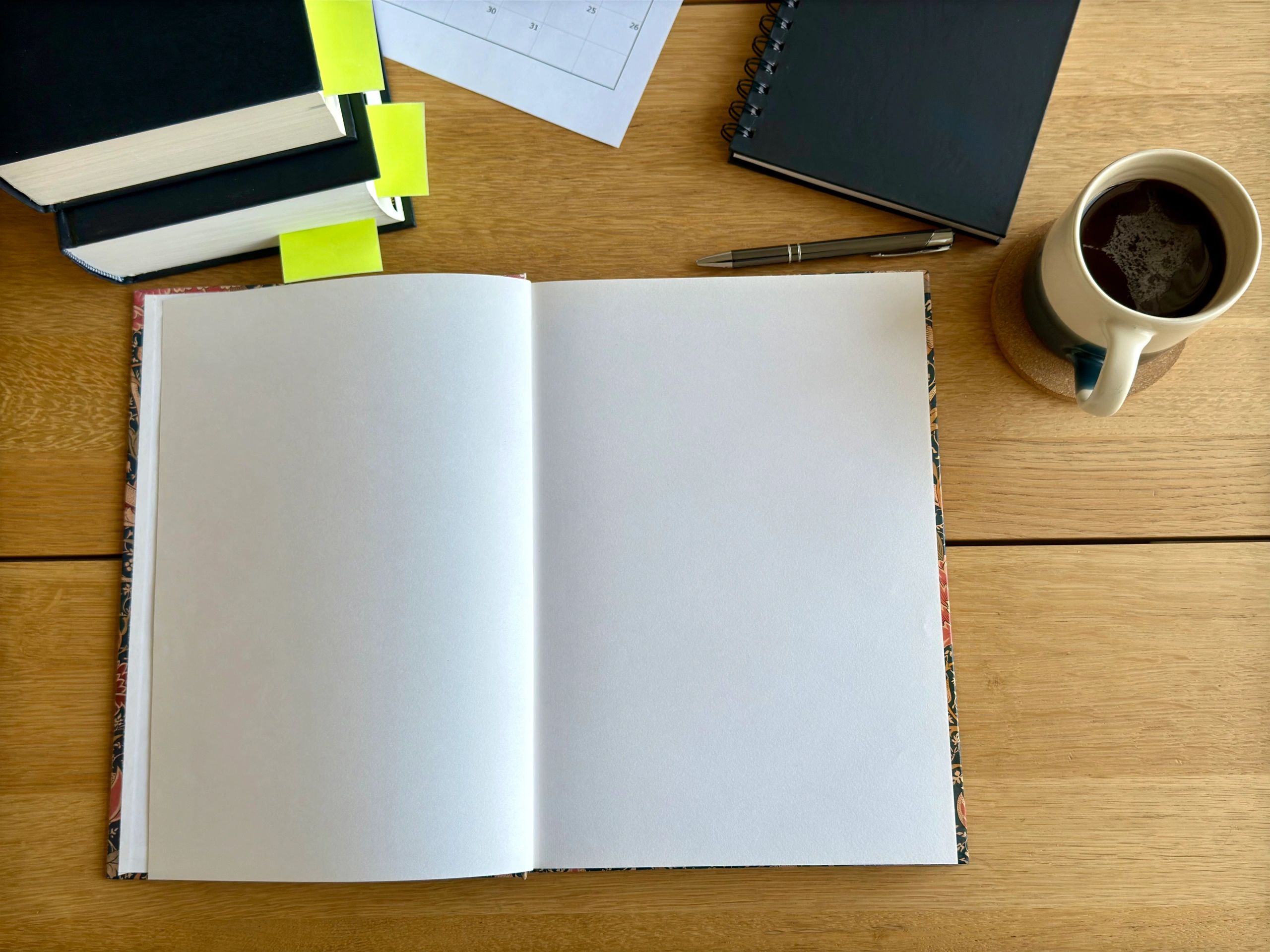 Open notebook on a wooden table with books and a mug nearby